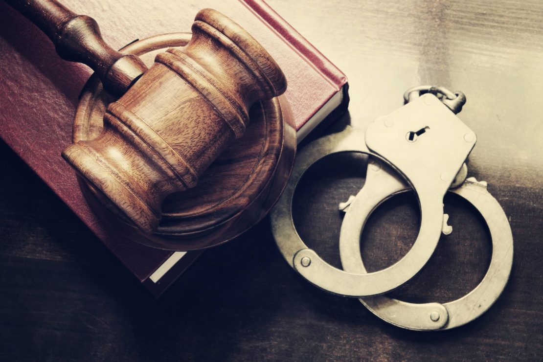 Gavel and handcuffs with red legal book on wooden table